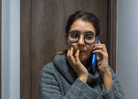 An anxious young female with glasses on the phone under the lights