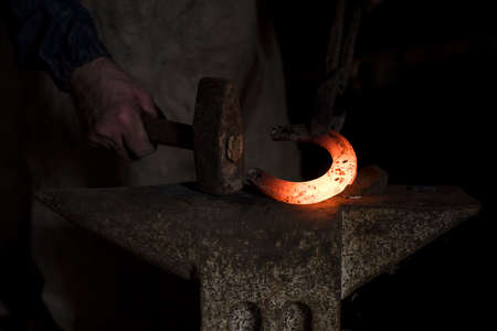 A closeup shot of the hands of a blacksmith hammering a hot horseshoeの写真素材
