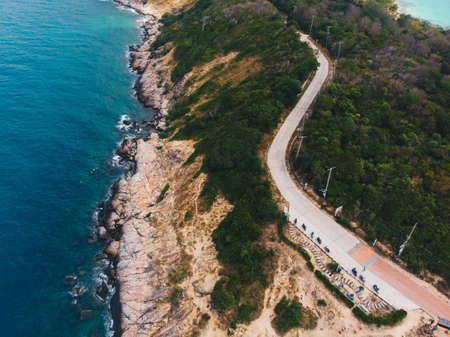 An aerial shot of a road in the middle of trees near the cliff and the sea