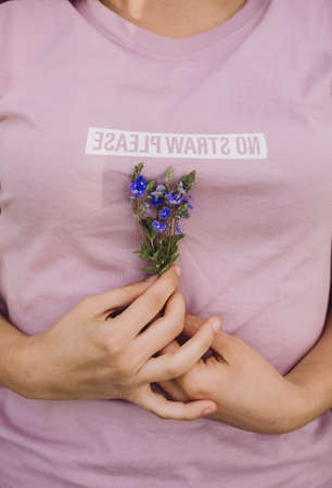 A selective closeup shot of a female with a purple shirt holding a blue-petaled flower during...