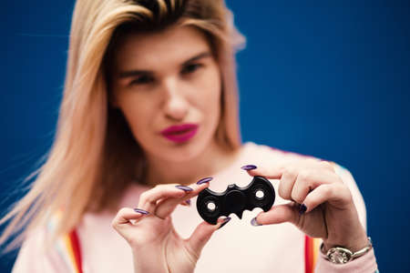An attractive female model posing on a blue background with a bat-shaped fidget spinner