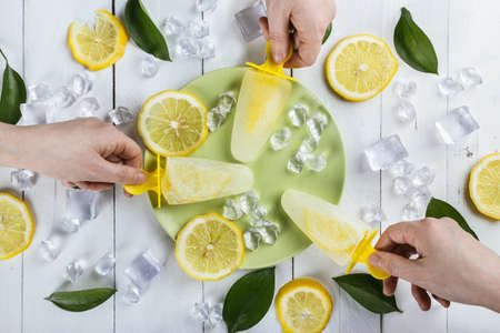 A closeup high angel shot of three hands holding lemon over a green plate with ice and slices of lemon aroundの写真素材