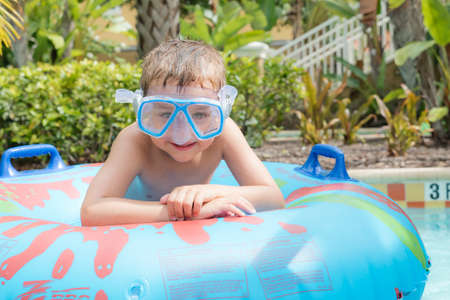 A young boy in a swimsuit playing and having fun with an inflatable water ring at a pool near a...