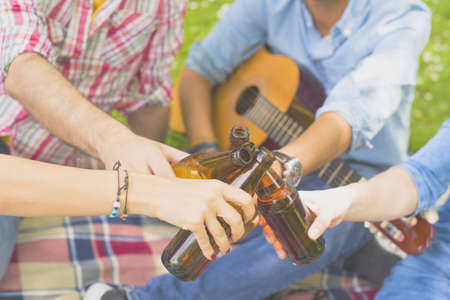 A closeup of a group of caucasian friends toasting with their beer bottles, in a park during daylightの写真素材