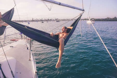 A horizontal shot of a male lying down on a hammock near the sea enjoying the warmth of the sunの写真素材
