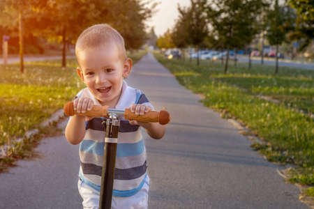 A picture of a happy kid riding a scooter in a parkの写真素材