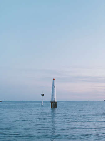 A vertical shot of a white lighthouse on the body of the waterの写真素材