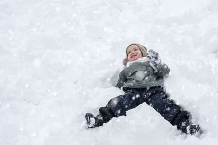 A little Caucasian boy lying on his back in the snow and enjoying snowfallの写真素材