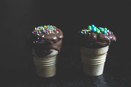 A black surface with two chocolate ice-cream cones with sprinkles on top