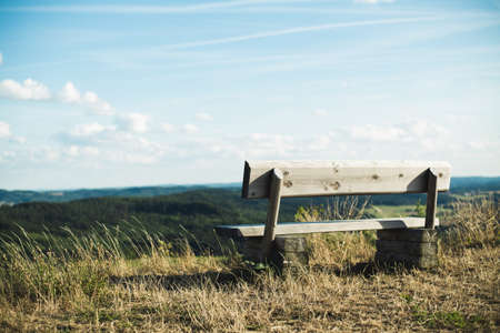 A wooden bench on a hill with a breathtaking view of the tree covered hills under the blue skyの写真素材