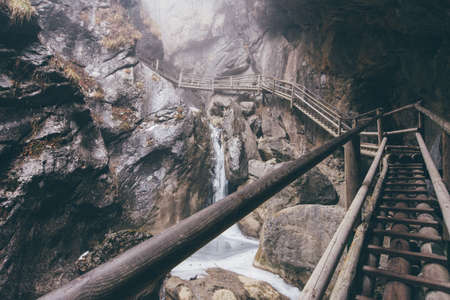 A beautiful shot of a wooden cliff path leading up the mountain with a small waterfall underneathの写真素材