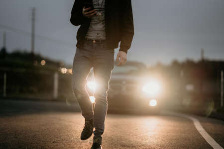 A stylish male walking on the road with vehicle's projectors lighting the wayの写真素材