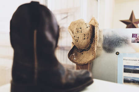 A selective closeup shot a black cowboy boot near brown straw hat on a wallの写真素材