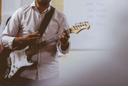 A selective focus shot of a male playing an electric guitar with a blurred backgroundの写真素材
