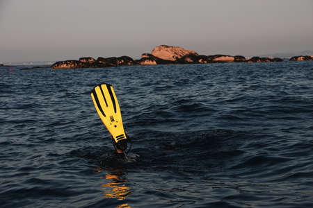 A beautiful shot of divers feet above the water with rocks and a cloudy sky in the background