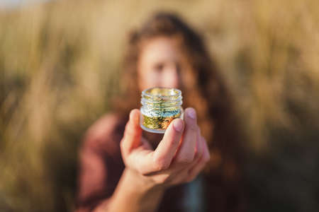 A selective focus shot of a model holding a glass full of golden glitterの写真素材
