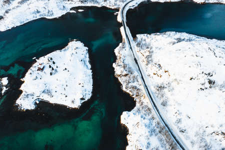 A bird's-eye shot of a road going through snowy islands on a body of water