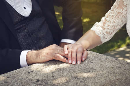 A closeup shot of a bride and a groom holding hands over a wooden surfaceの写真素材