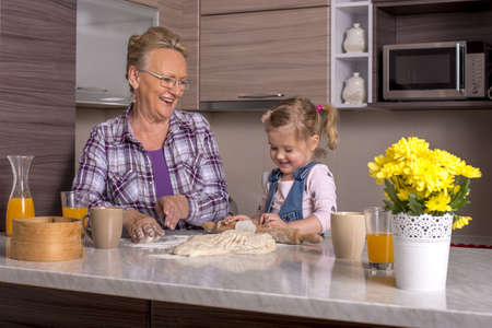A happy Caucasian grandmother and granddaughter having fun making dough in the kitchen