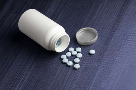 A closeup shot of round pills on the table behind the white containerの写真素材