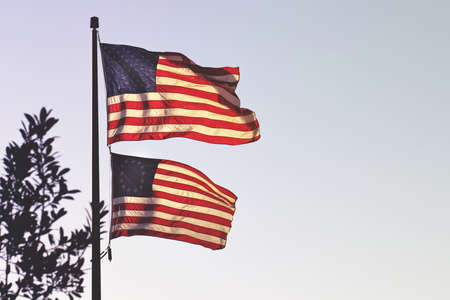Two American flags waving on a single metal pole on a bright sunny dayの写真素材
