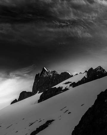 A greyscale low angle shot snowy rocks under the sky with huge grey clouds in winterの写真素材