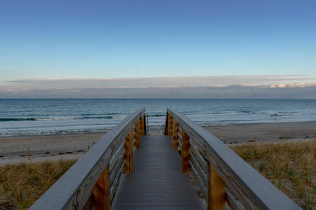 A relaxing scene of a wooden bridge leading to the wild seashore with a calm evening sky in the...