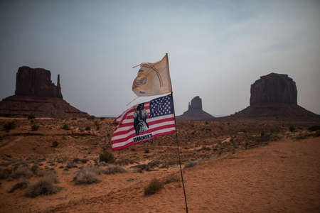 A horizontal shot of the flag of US with a Geronimo print in front of beautiful rock formations in Monument Valley, USAの写真素材