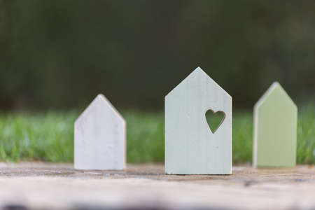 Three small wooden houses with a heart on the big one symbolizing family love and security at homeの写真素材