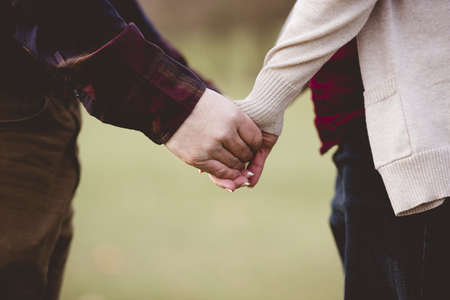 A closeup shot of a couple holding hands with a blurred backgroundの写真素材