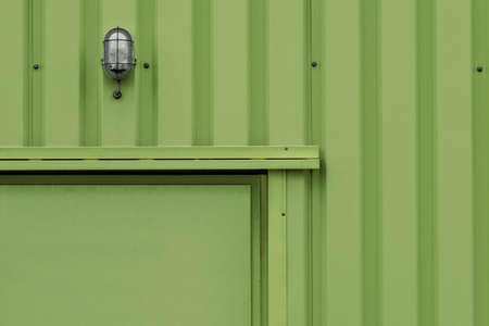 A horizontal closeup shot of a green metal background with a lamp on the wallの写真素材