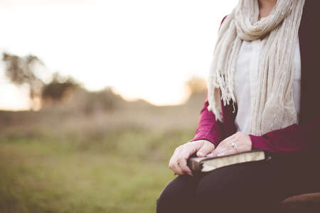 A closeup shot of a female sitting while holding the bible with a blurred background