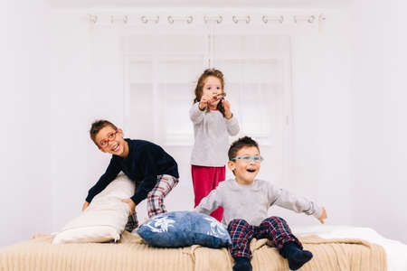 The three cheerful children with glasses jumping and playing on the bed
