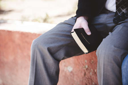 A closeup shot of a male sitting and holding the bible with a blurred backgroundの写真素材