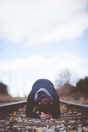 A vertical shot of a male down on the ground on train track praying with a blurred backgroundの写真素材