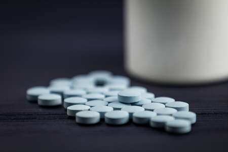 A closeup shot of round pills on the table behind the white containerの写真素材