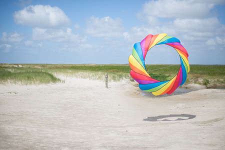 A beautiful shot of a person holding a colorful round kite in the sandy shore under the calm skyの写真素材