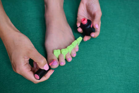 A closeup shot of a female with a toe separator painting her toenails with pink polishの写真素材