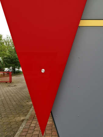 A low angle shot of a triangle-shaped red banner on a grey wall with a yard scene on the left