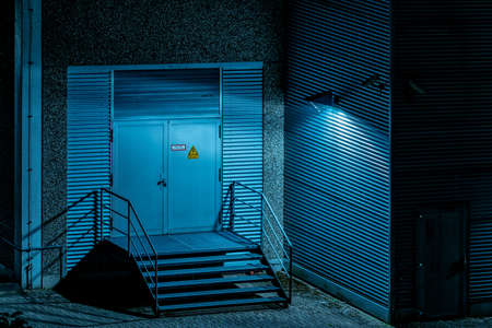 A horizontal shot of a door with a warning sign near the metal staircases covered with a lantern light at nighttimeの写真素材