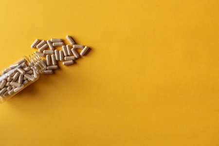 The pills scattered out of an open bottle on a yellow backgroundの写真素材