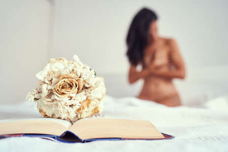 A closeup of a bouquet of dried flowers on an open book on the bed with a naked female on the backgroundの写真素材