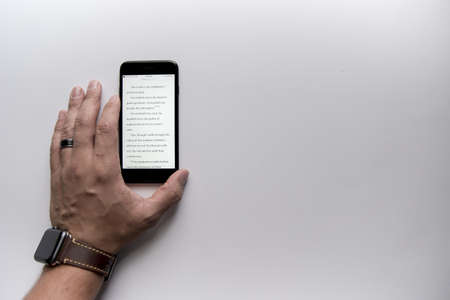 An overhead shot of a male hand near his smartphone on a white surface