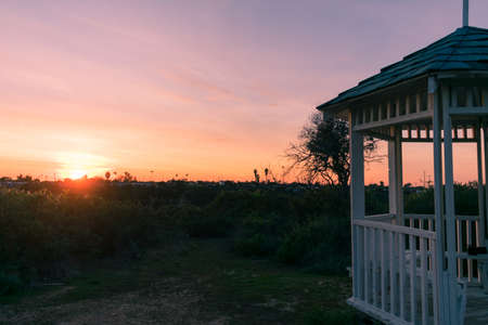 A horizontal shot of a white gazebo pavilion structure in a green grassy field during sunset.の写真素材