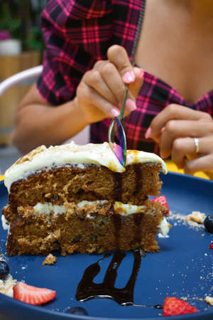 A vertical closeup shot of a spoon cutting a slice of carrot cake on a blue plateの写真素材