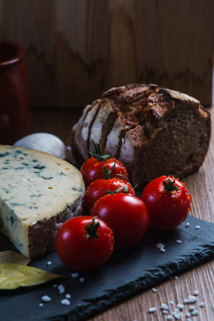 A vertical shot of a Roquefort cheese next to tomatoes and bread