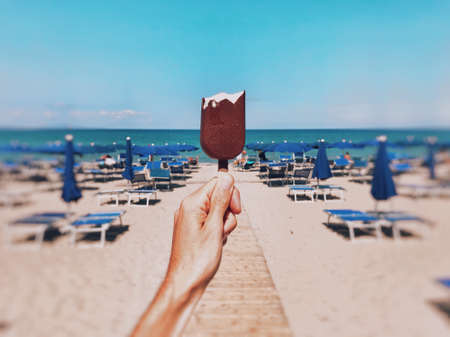 A horizontal shallow focus closeup shot of a person holding a bitten chocolate ice-cream on the beach with a blurred backgroundの写真素材