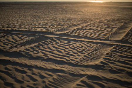 A high angle shot of a sandy shore with huge traces of a car and the sun shining in the backgroundの写真素材
