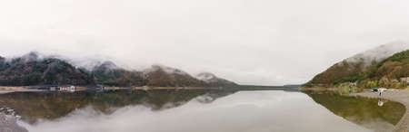 A panoramic shot of water surrounded by mountains under a cloudy sky