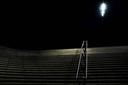 A horizontal nighttime shot of wide stairs with handrails going up and a turned-on lamppost